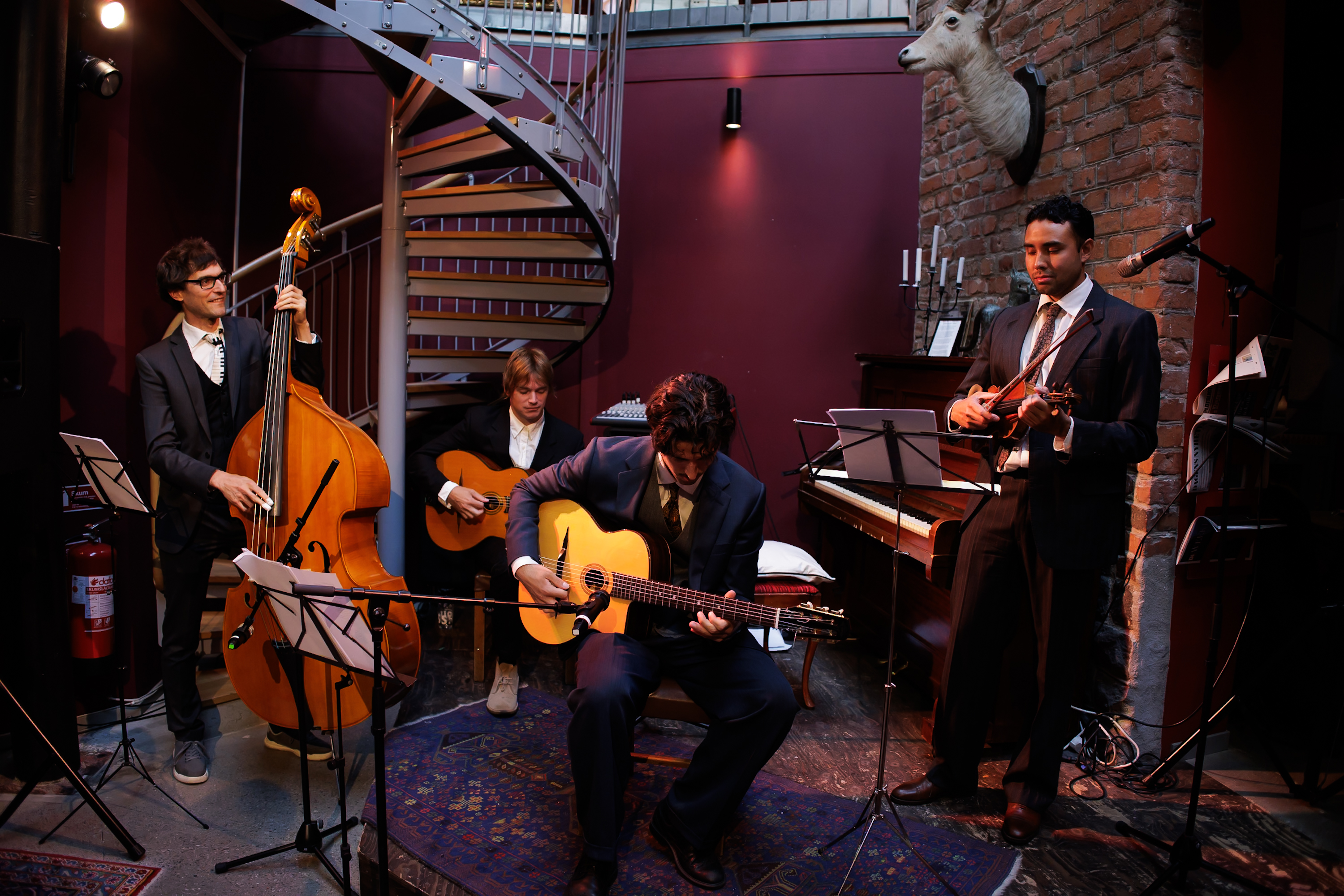 The Django Quartet spelar live i klubbmiljö, med den spiralformade trappan och tegelväggen i bakgrunden.